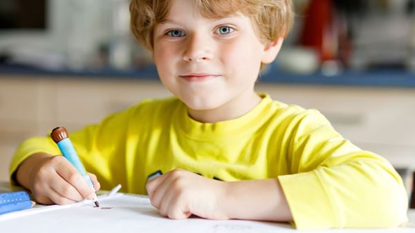 young smiling boy in yellow shirt drawing