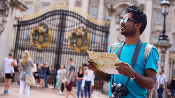 bespectacled man consulting map in front of buckingham palace gates